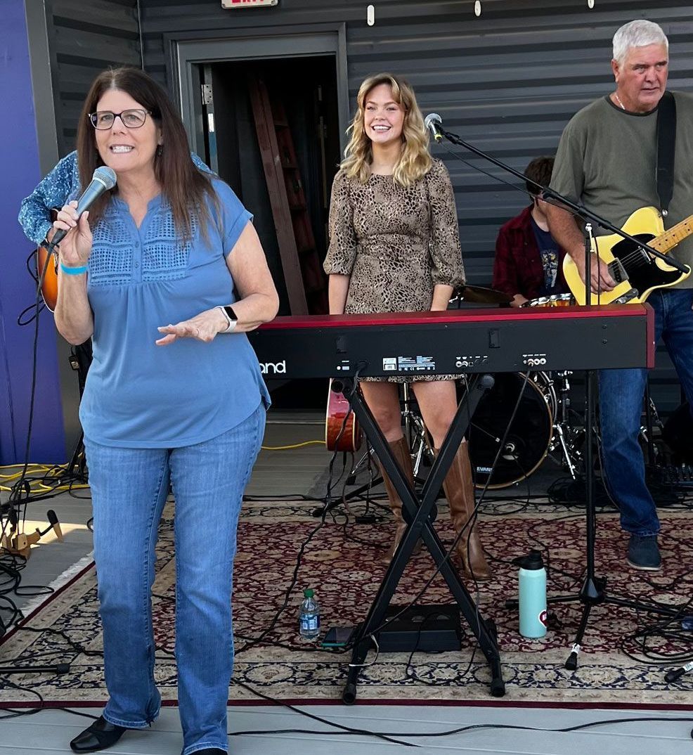 A woman is singing into a microphone while standing in front of a keyboard.