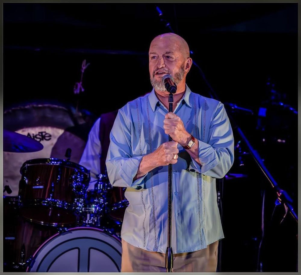 A bald man singing into a microphone on a stage