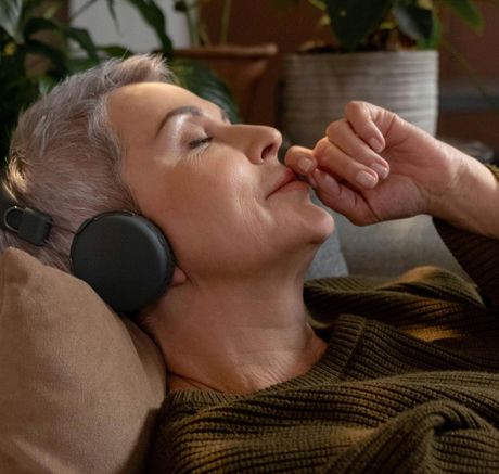 A woman is laying on a couch wearing headphones.