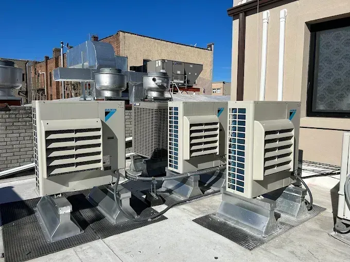 Rooftop with three air conditioning units, metal ductwork, and a clear blue sky.