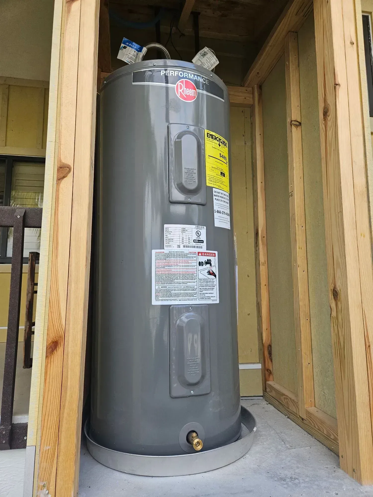 Gray water heater enclosed in wooden framing, outdoors.