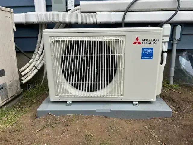 Mitsubishi Electric heat pump on a concrete pad outside a blue building.