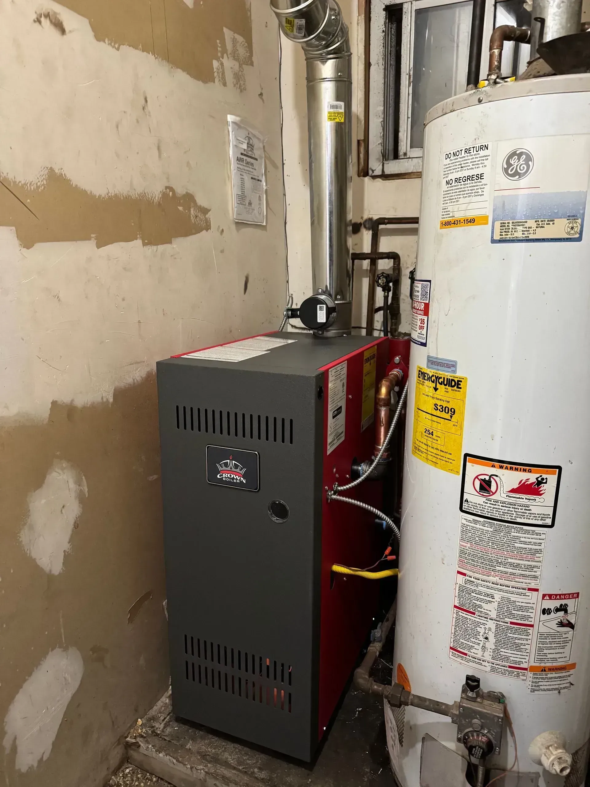 Oil furnace and water heater in a utility room with exposed wall.