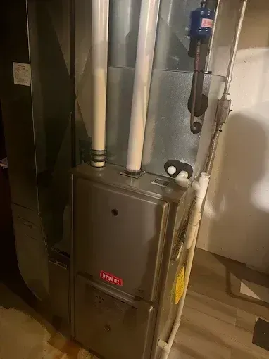 Furnace unit with metal ducts and pipes in a room. Gray metal and white pipes.