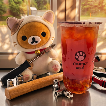 A Rilakkuma plush in a cat costume holds a screwdriver next to a Momo Ashi bubble tea cup and various metal tools.