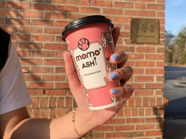 A hand holds a pink disposable cup labeled 