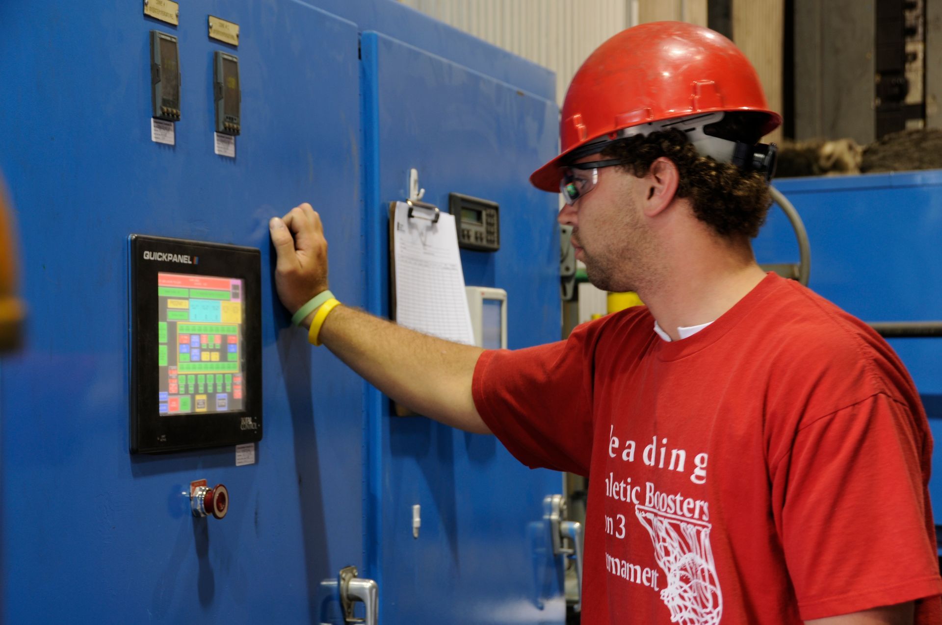 Man in red shirt operating heat treat machine.