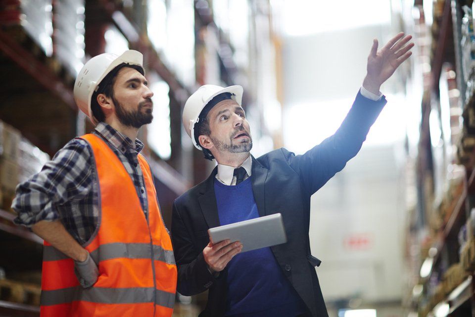 businessman with touchpad pointing at upper shelf with goods