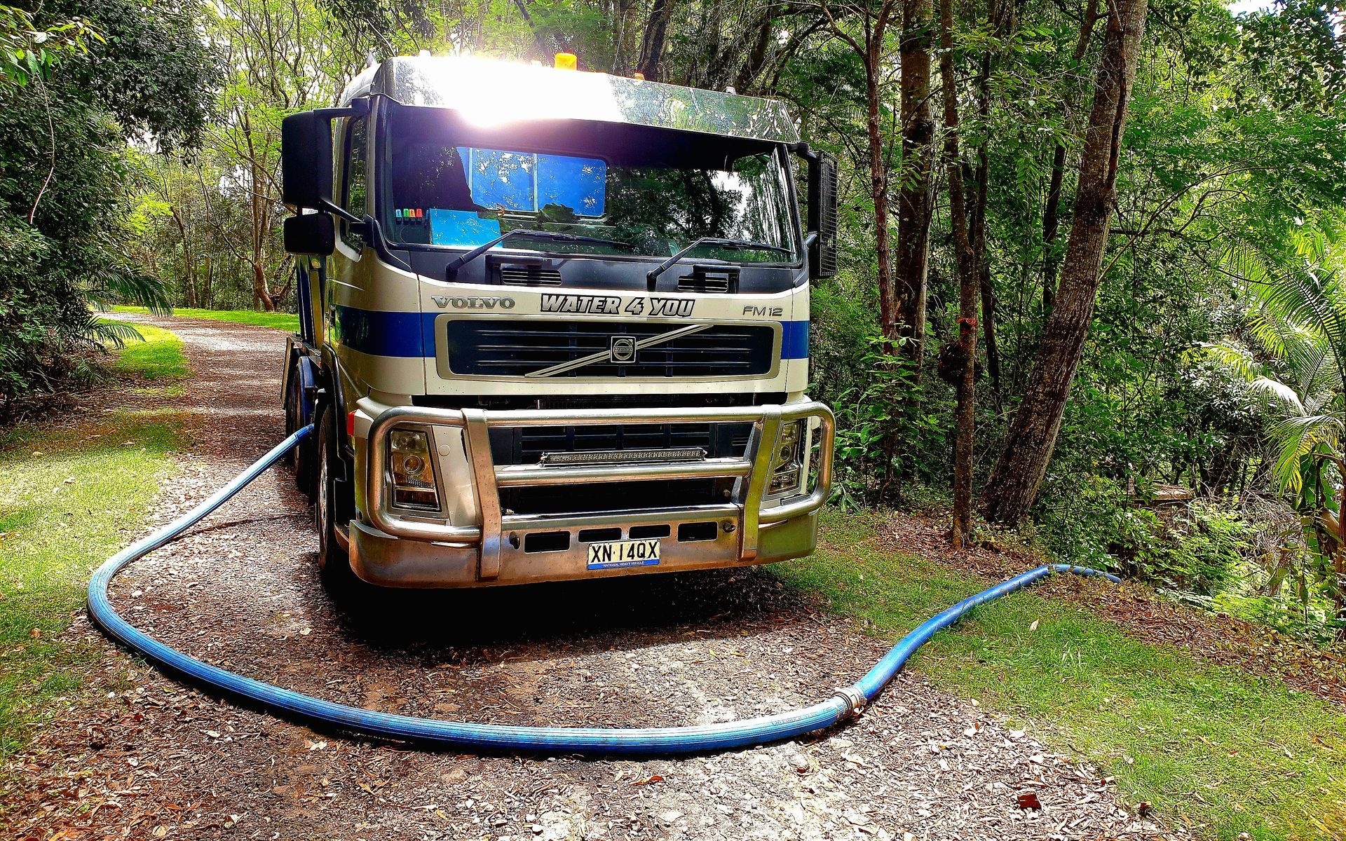 A Large Orange Truck With a Blue Tarp on the Back is Parked in a Grassy Field — Water 4 You In Clovass, NSW