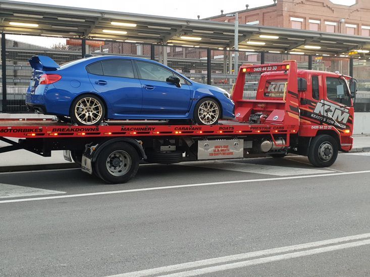 A Blue Car Is Being Towed By A Red Tow Truck — KTM Towing In Crescent Head, NSW