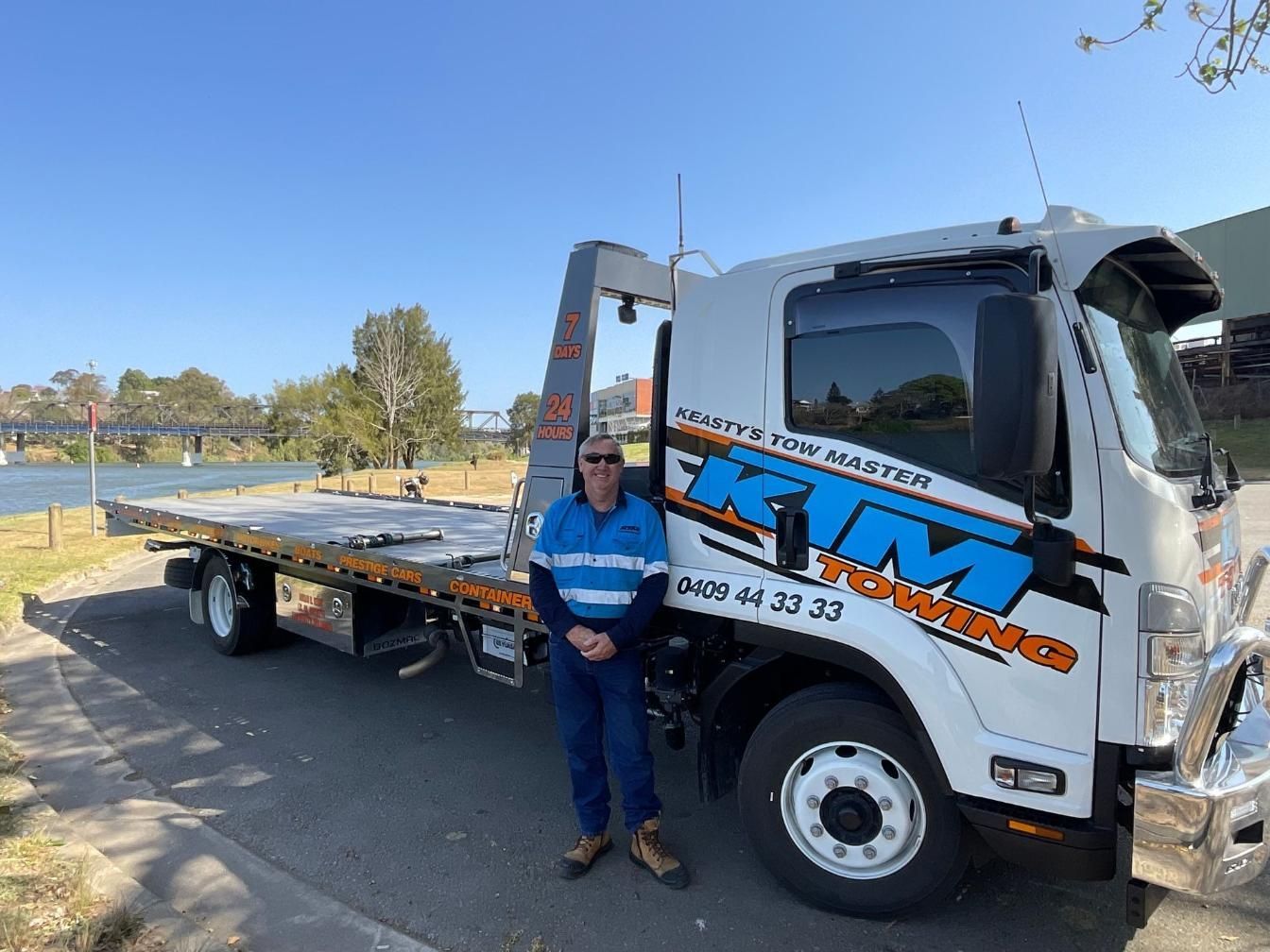 A Man Is Standing In Front Of A Tow Truck — KTM Towing In Crescent Head, NSW
