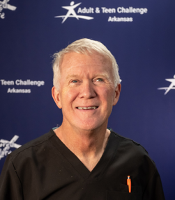 A man stands in front of a blue background that says adult & teen challenge arkansas