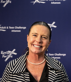 A woman is smiling in front of a sign that says adult & teen challenge