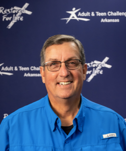A man wearing glasses and a blue shirt stands in front of a restore for life sign