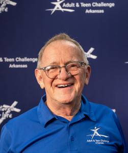 A man wearing glasses and a blue shirt that says adult & teen challenge