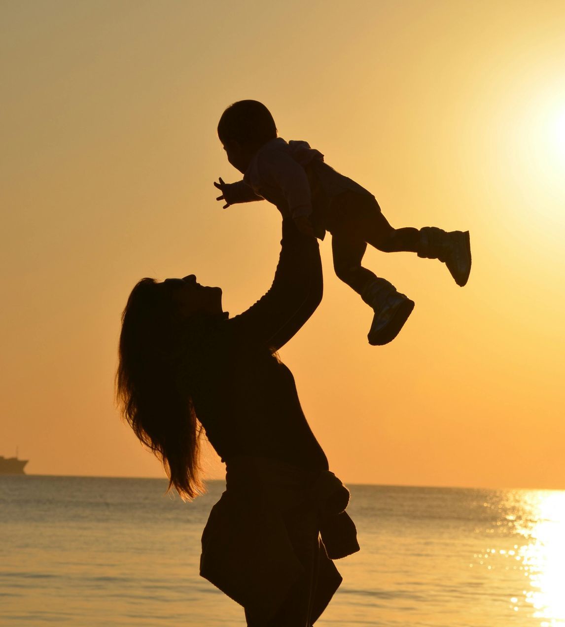 A silhouette of a woman holding a baby in the air