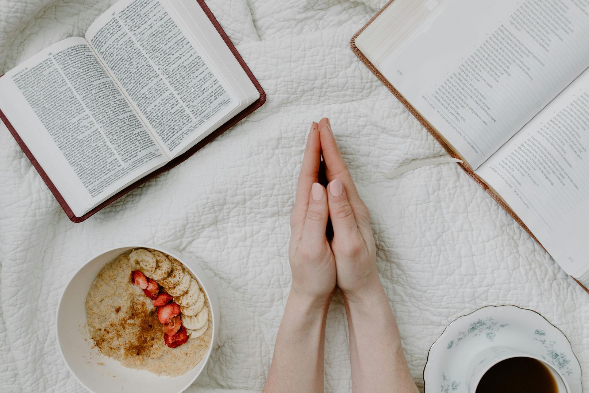 A person is praying in front of a bowl of food and a bible.
