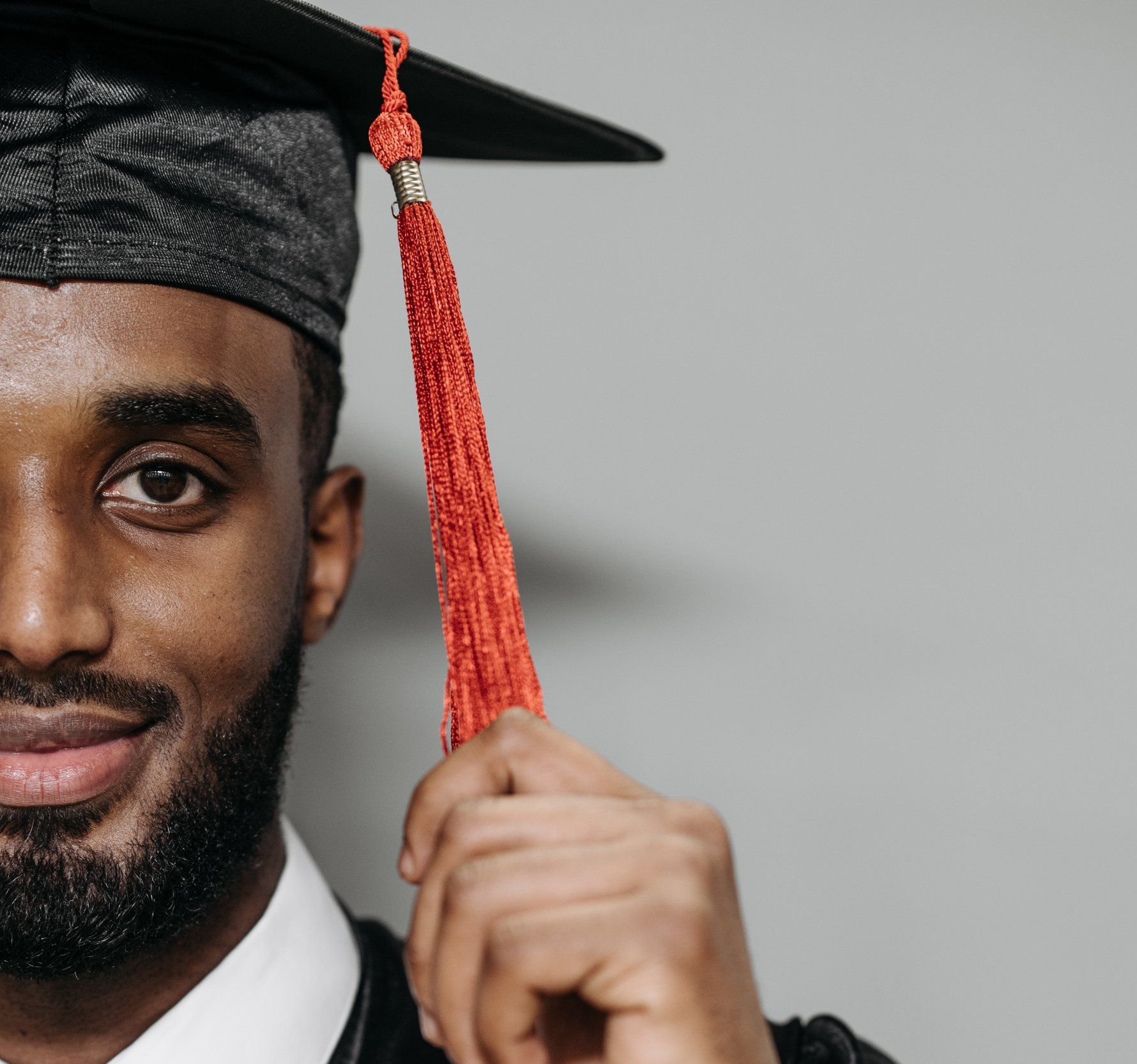 Alumni stories | graduate holding a red tassel on his grad cap.
