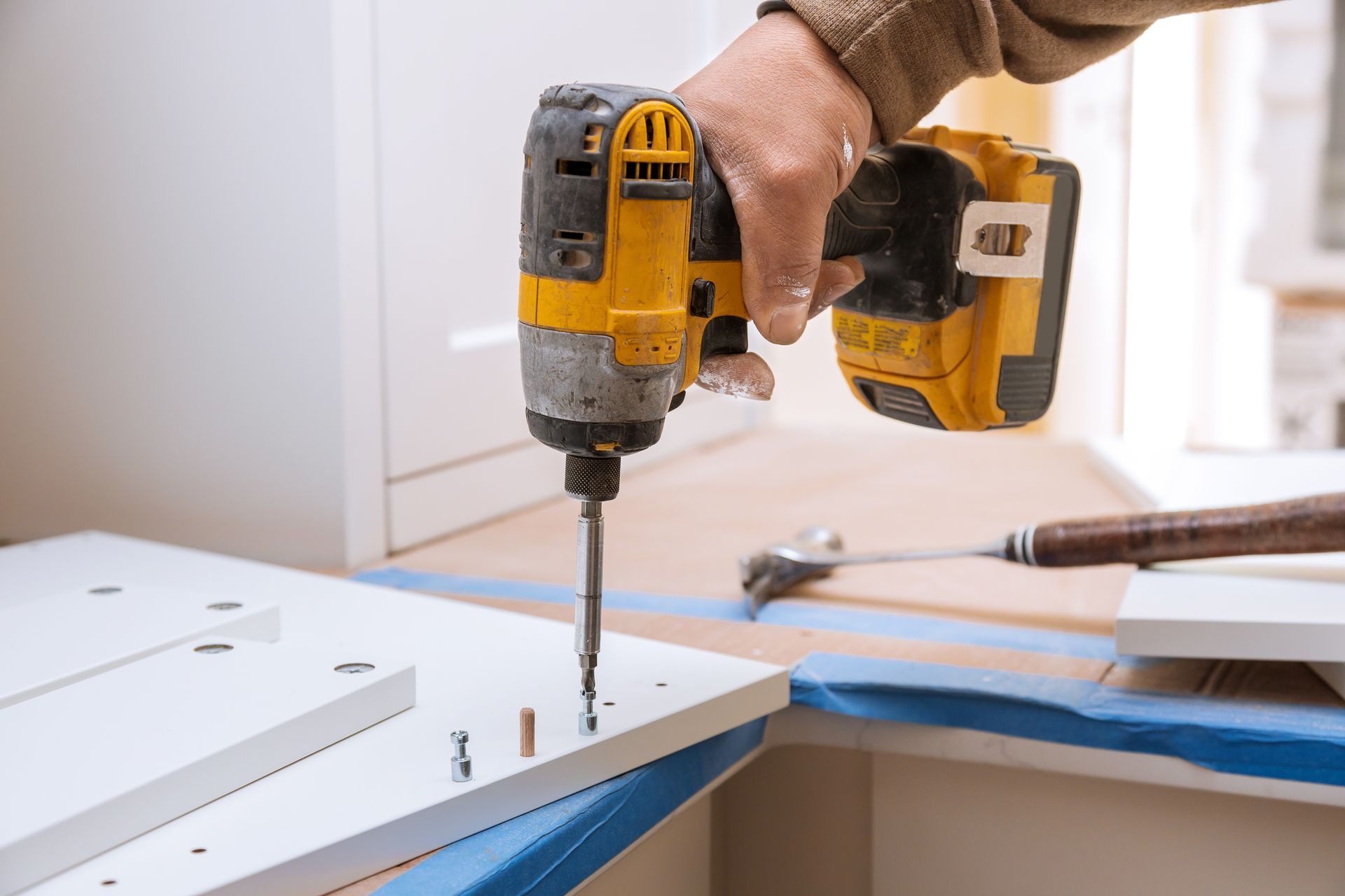Person using a yellow and black power drill to assemble white cabinet components.
