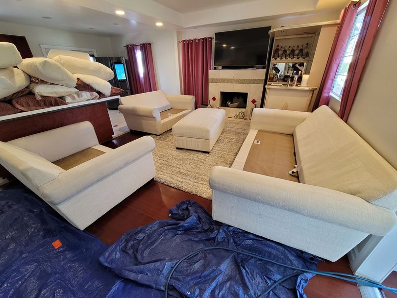 Cozy living room with cream sofas, a fireplace, TV, red curtains, and a blue tarp on the floor