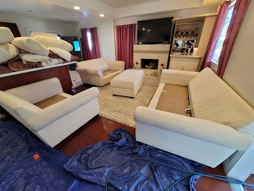 Living room with white sofas, armchairs, fireplace, rug, and TV in a cozy, cluttered interior.