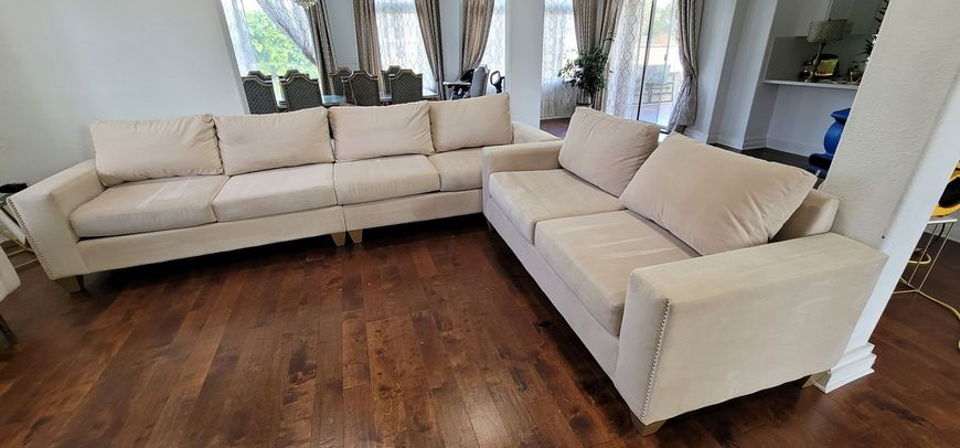 L-shaped beige sectional sofa in a bright living room with dark wood floors and large windows