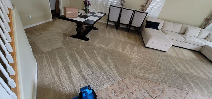 Spacious living room with beige carpet, sectional sofa, glass coffee table, and dining chairs in back.