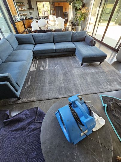 Gray sectional sofa in a sunroom, with a blue bag and dark bag on a round table in the foreground.