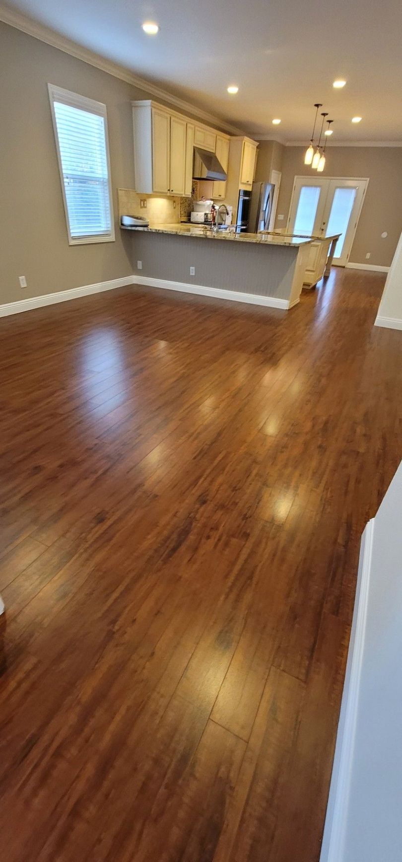 Empty living room with hardwood floors and an open kitchen area, lit by recessed ceiling lights.