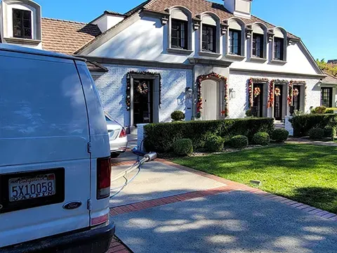 Blue van parked in front of a white suburban house with a manicured lawn and hedges