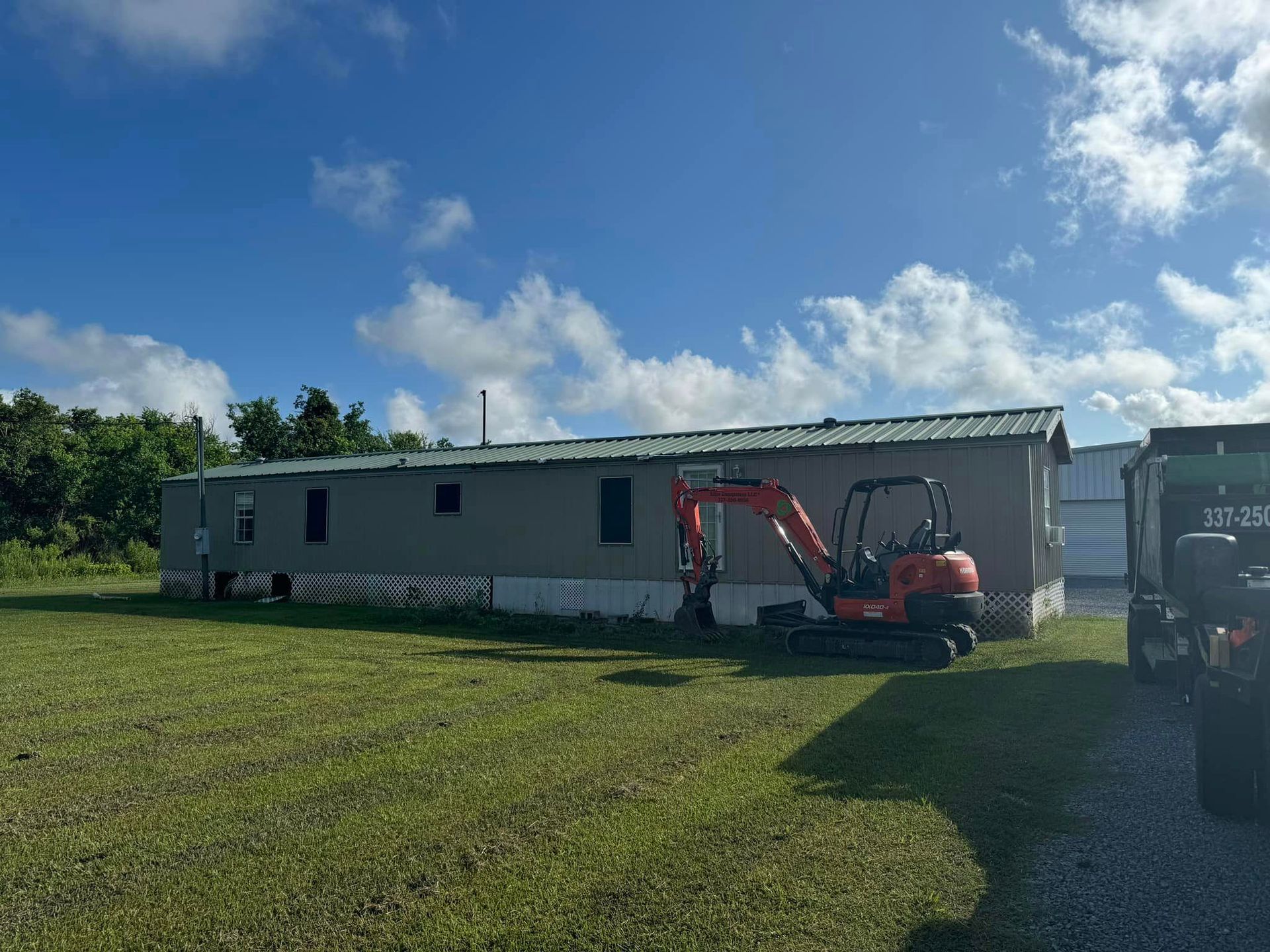 An excavator is digging a hole in the dirt in front of a house.