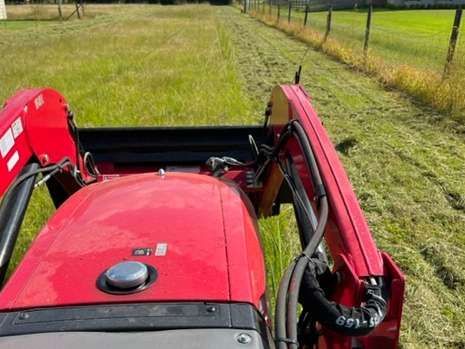 A red tractor is driving through a grassy field.