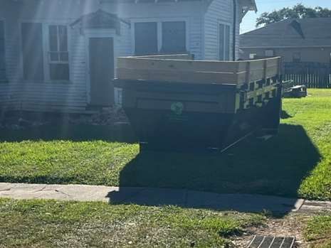 A trailer is parked in the grass in front of a house.