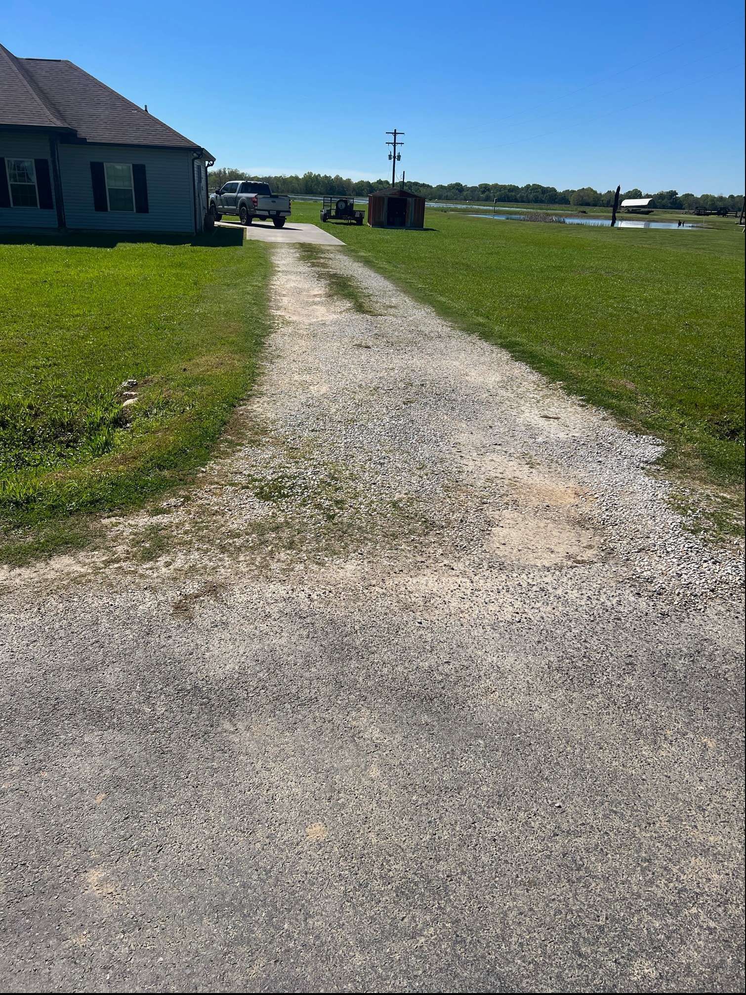 A dirt road leading to a house in the middle of a grassy field.