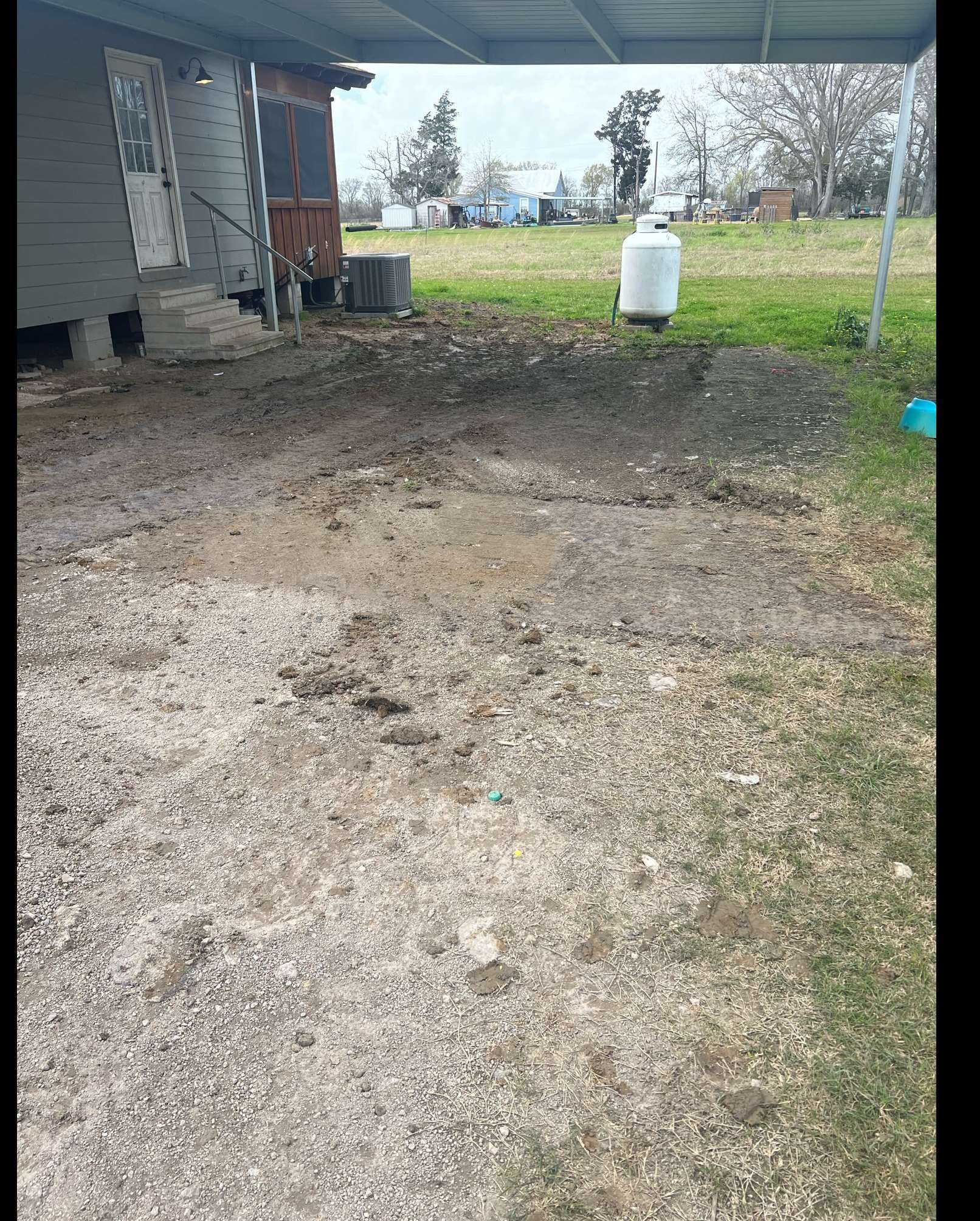 There is a propane tank in the dirt in front of a house.