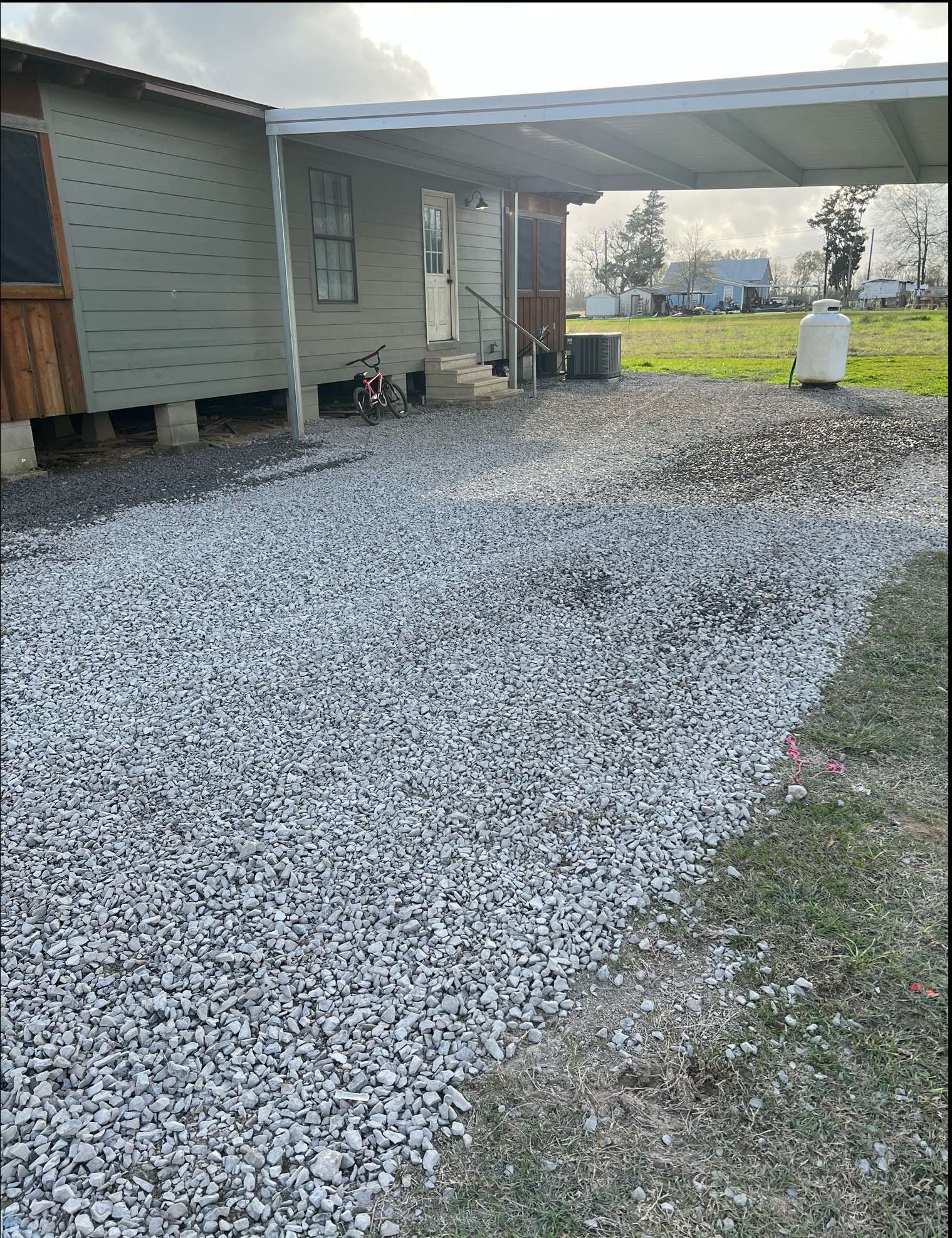 A house with a carport and gravel driveway in front of it.
