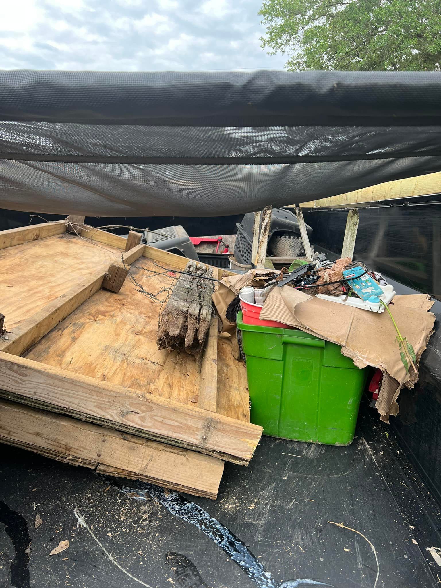 A green bin is sitting on top of a pile of wood in the back of a truck.
