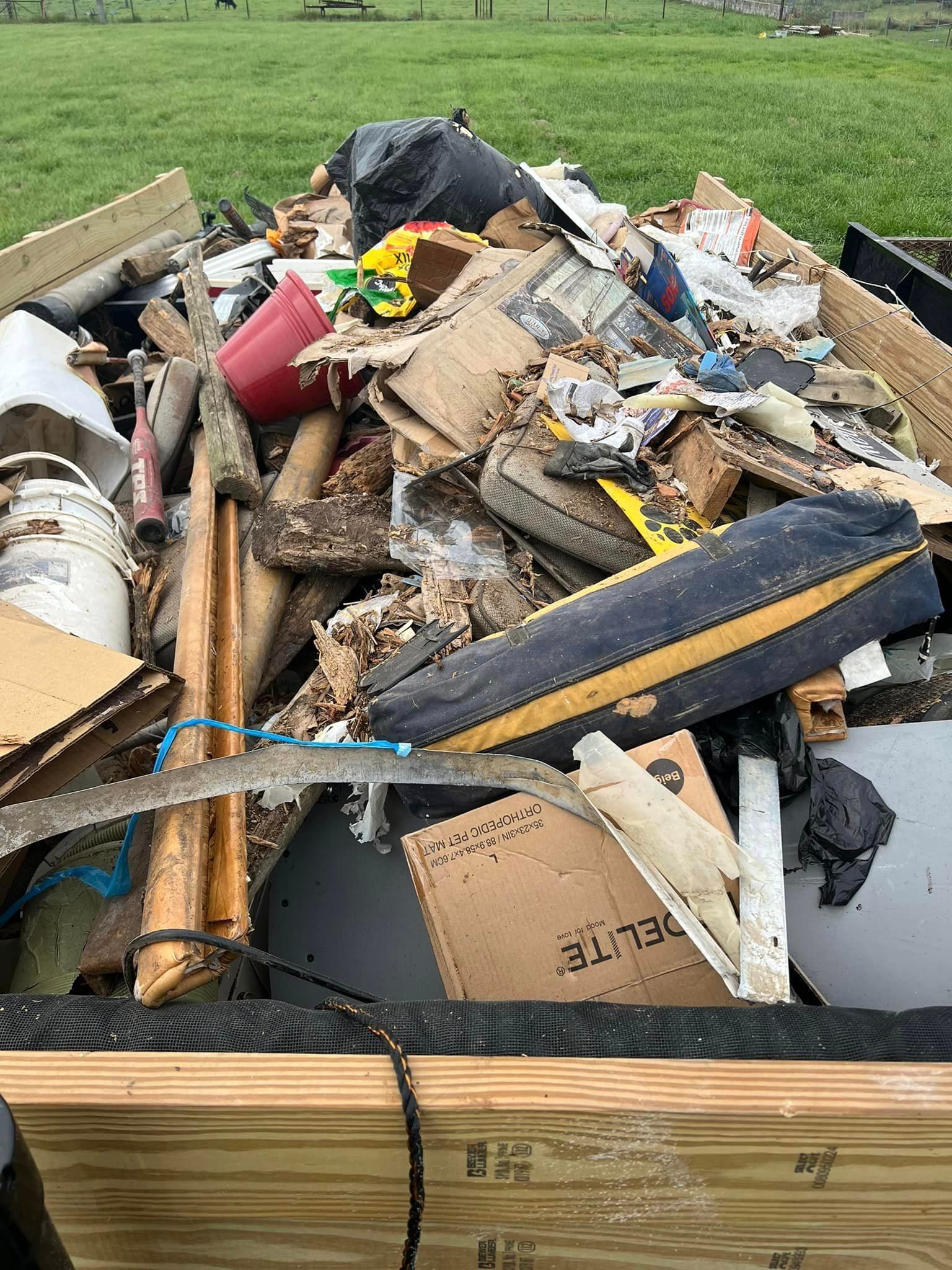 A pile of trash is sitting on top of a wooden pallet in a field.
