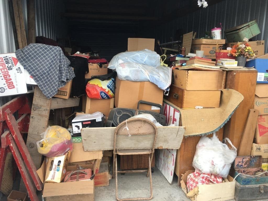A storage shed filled with lots of boxes and a chair.