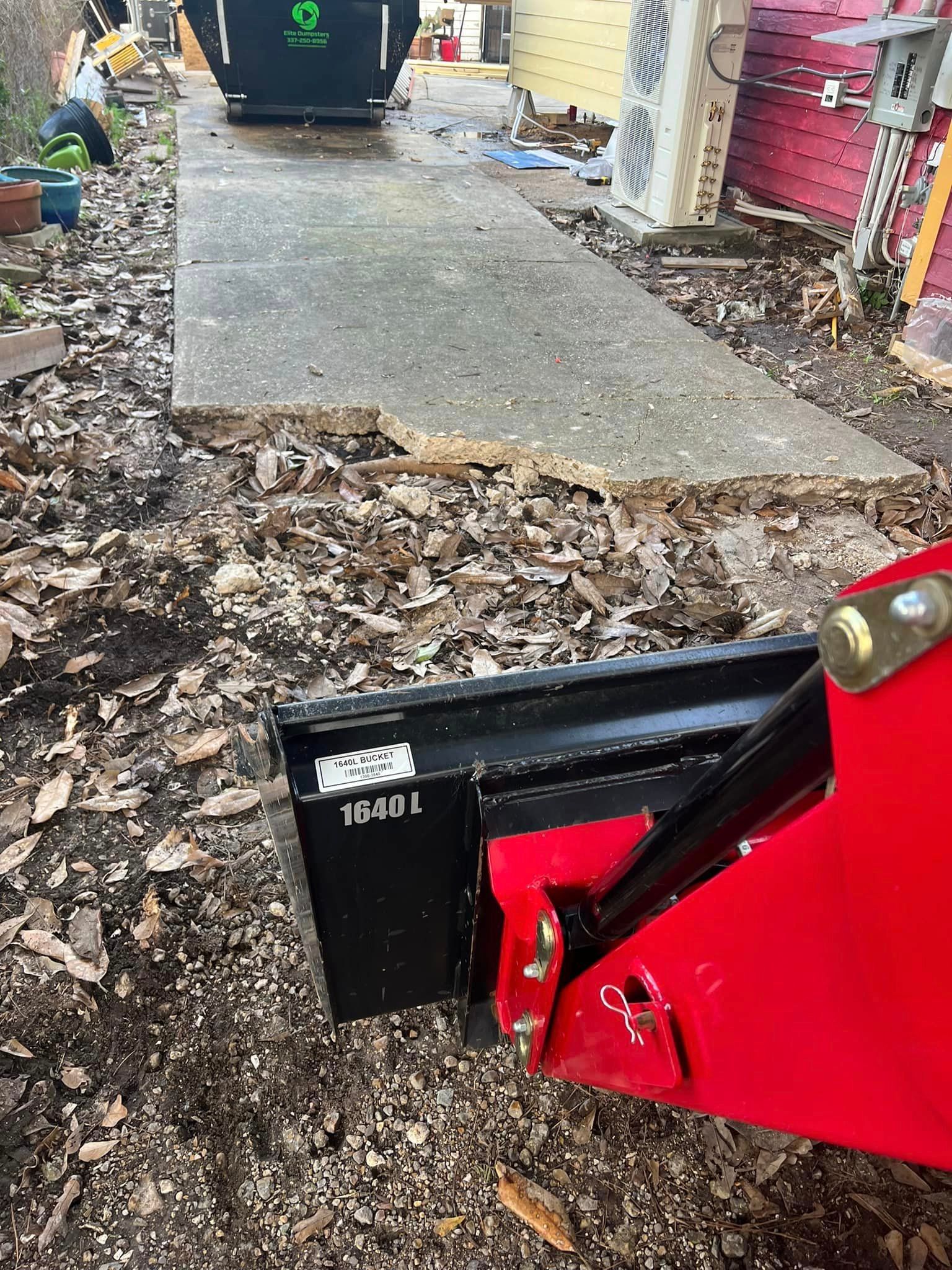A red and black object is sitting on the ground next to a sidewalk.