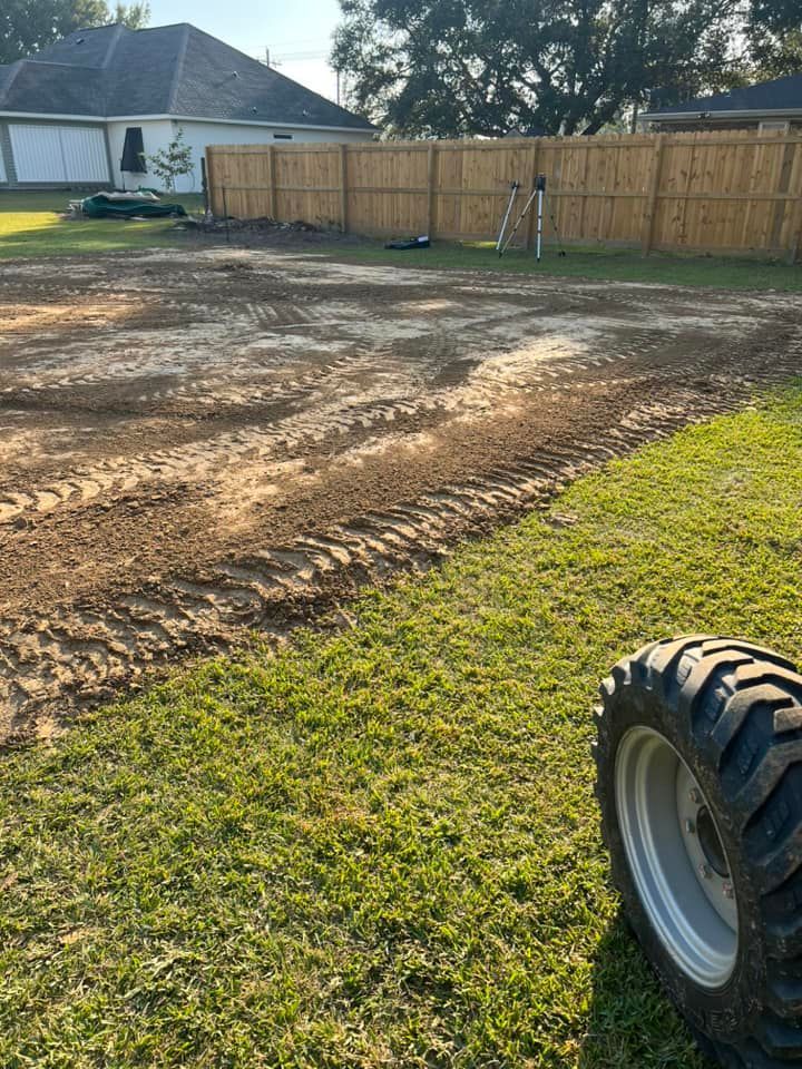 A tractor tire is sitting in the grass next to a dirt field.