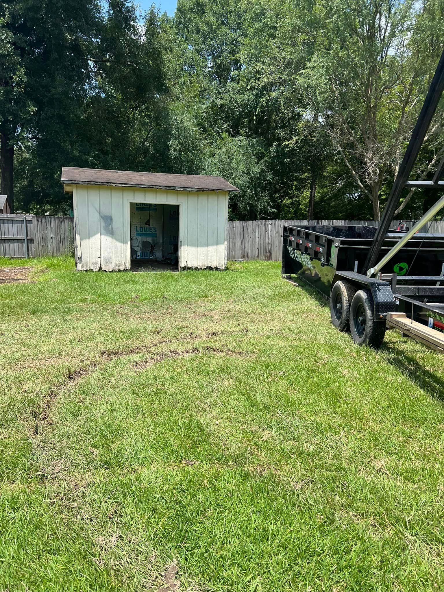 A trailer is parked in a grassy yard next to a shed.