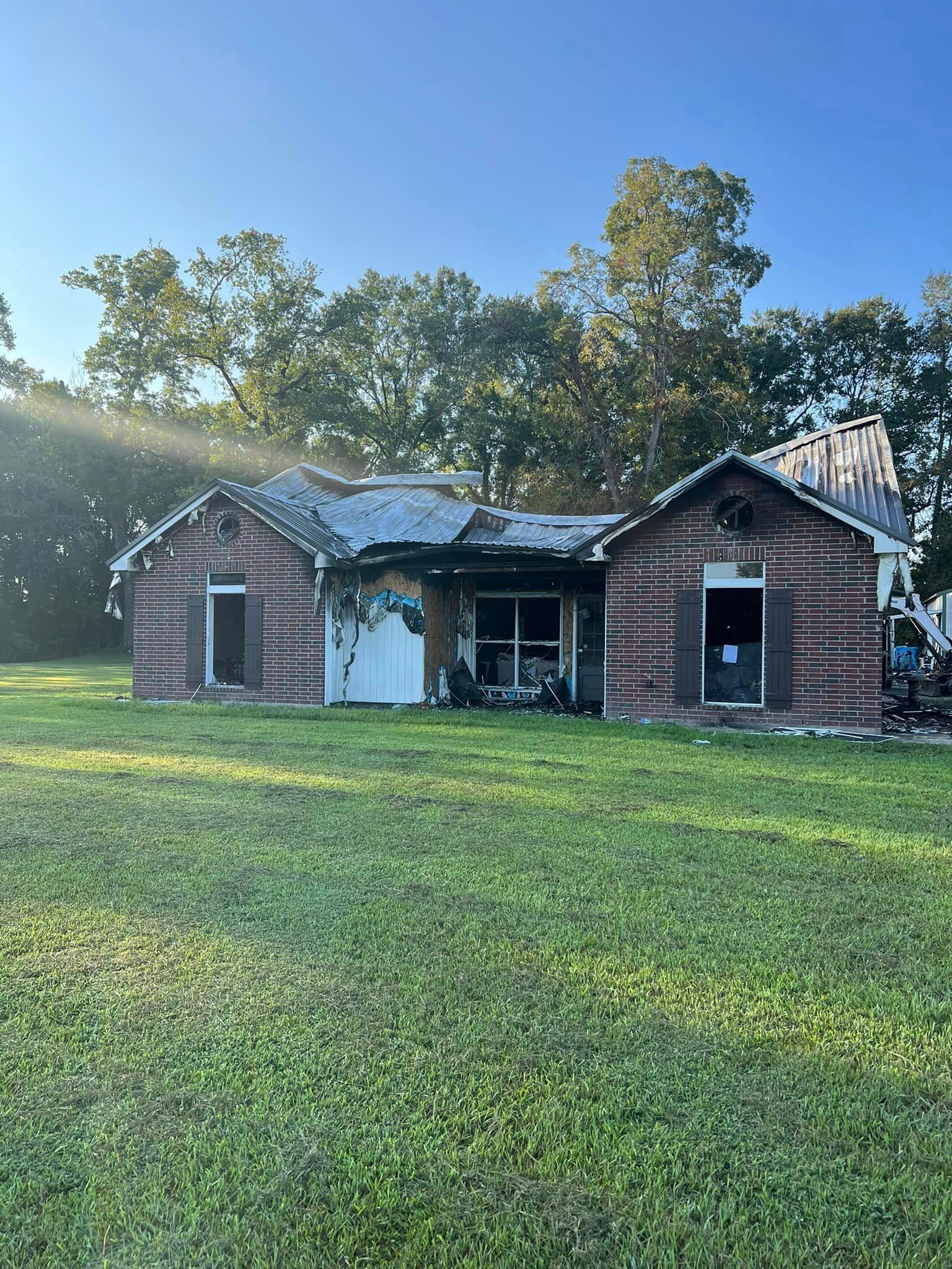 A brick house is sitting in the middle of a lush green field.
