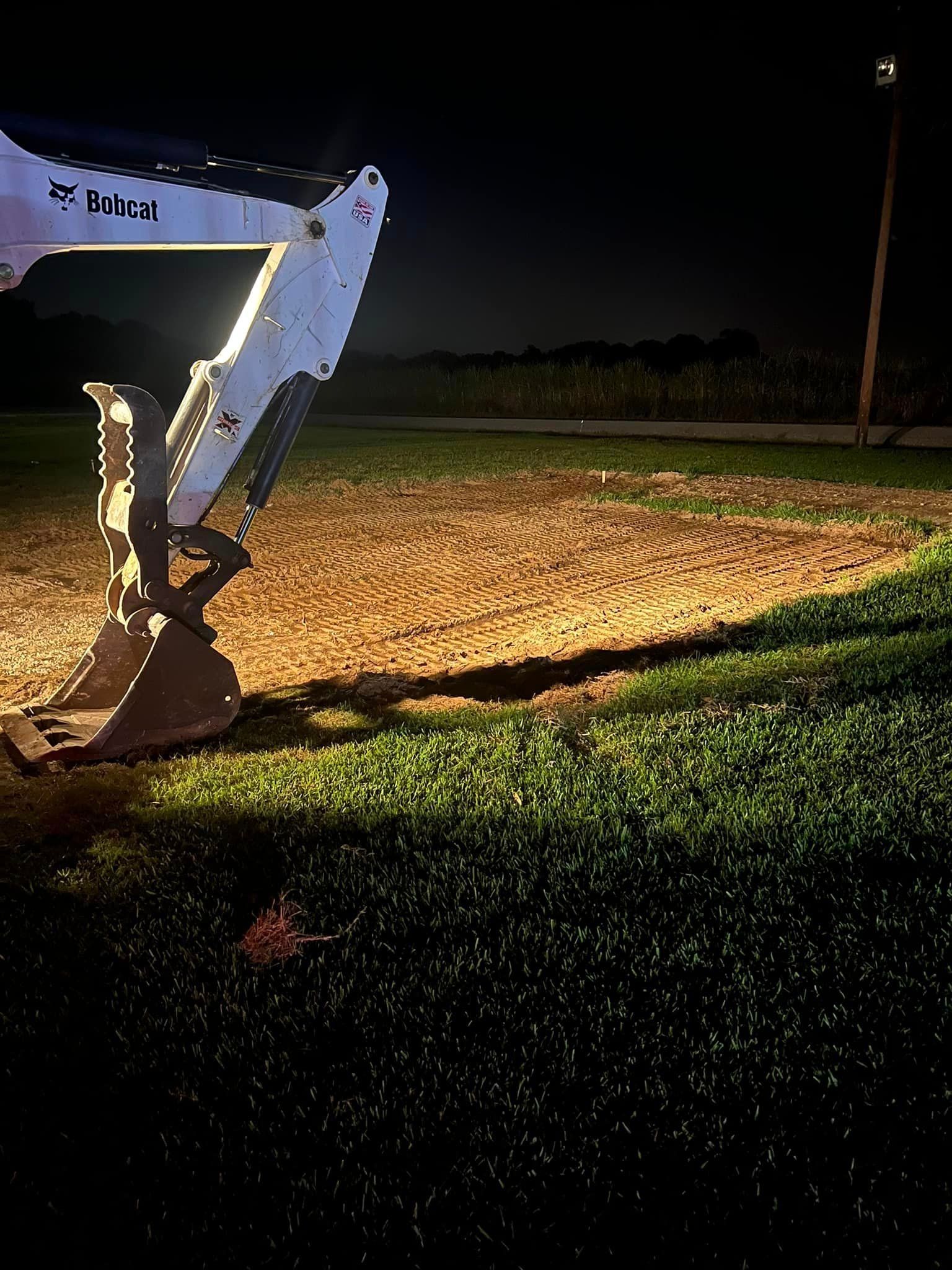 A bobcat excavator is working on a dirt field at night.