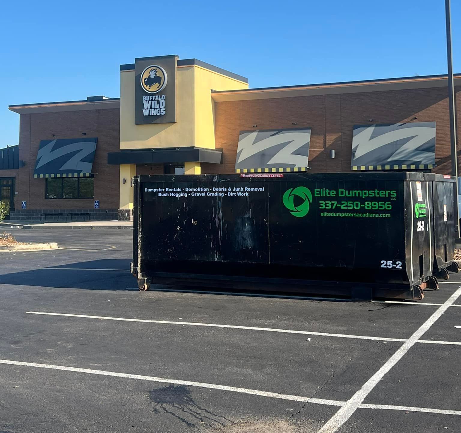 A dumpster is parked in front of a wing wing restaurant
