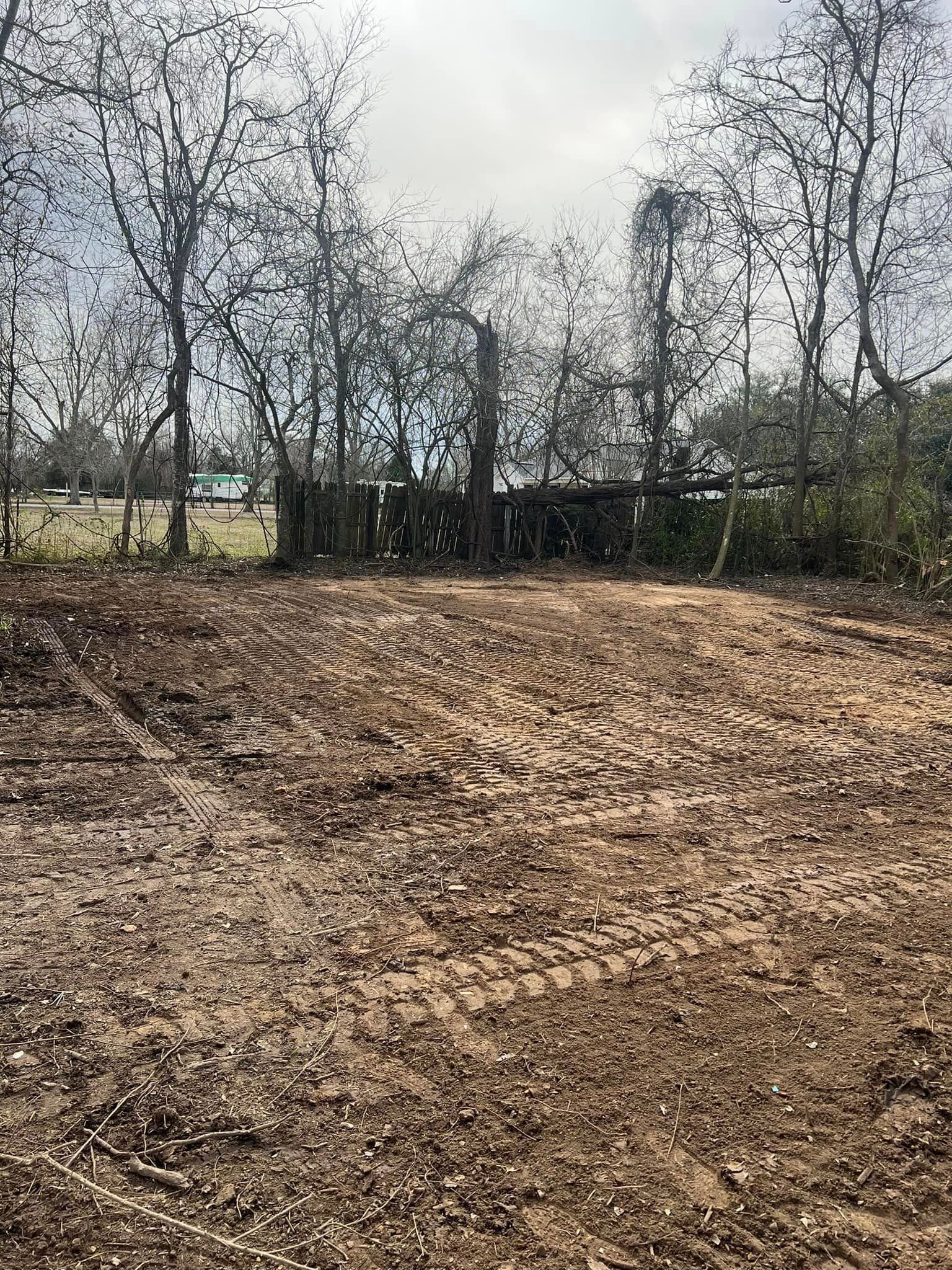 A dirt field with trees in the background and a fence in the background.