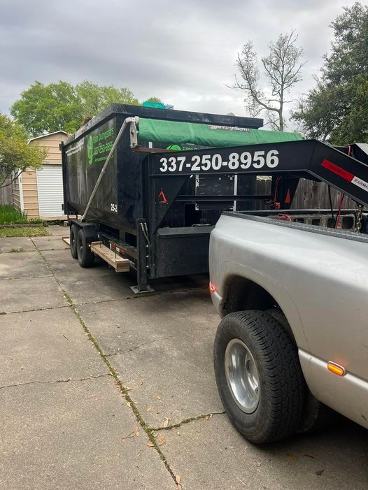 A dumpster is being towed by a truck in a driveway.