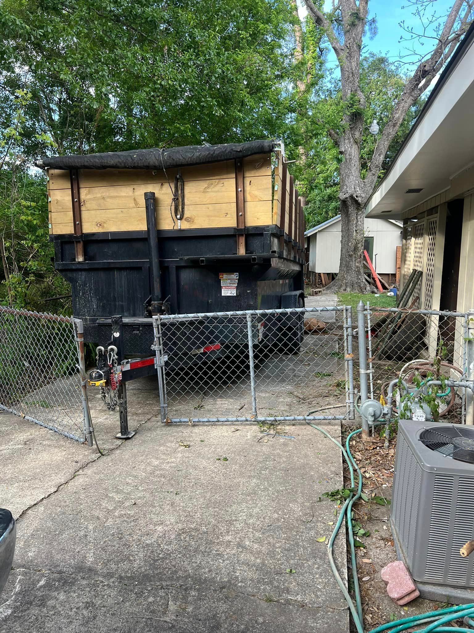 A dumpster is parked in front of a house behind a chain link fence.