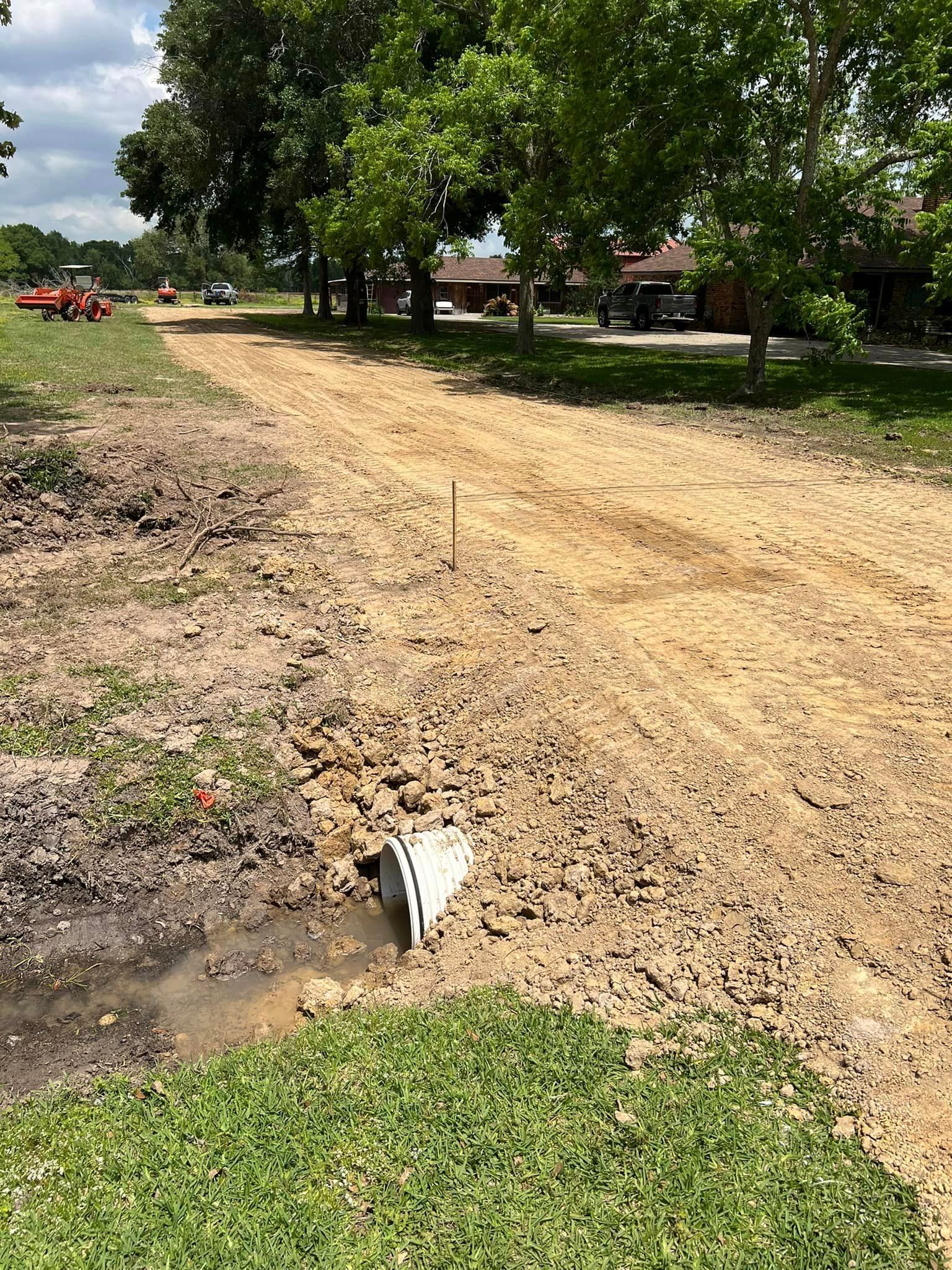 A dirt road going through a grassy field with trees in the background.
