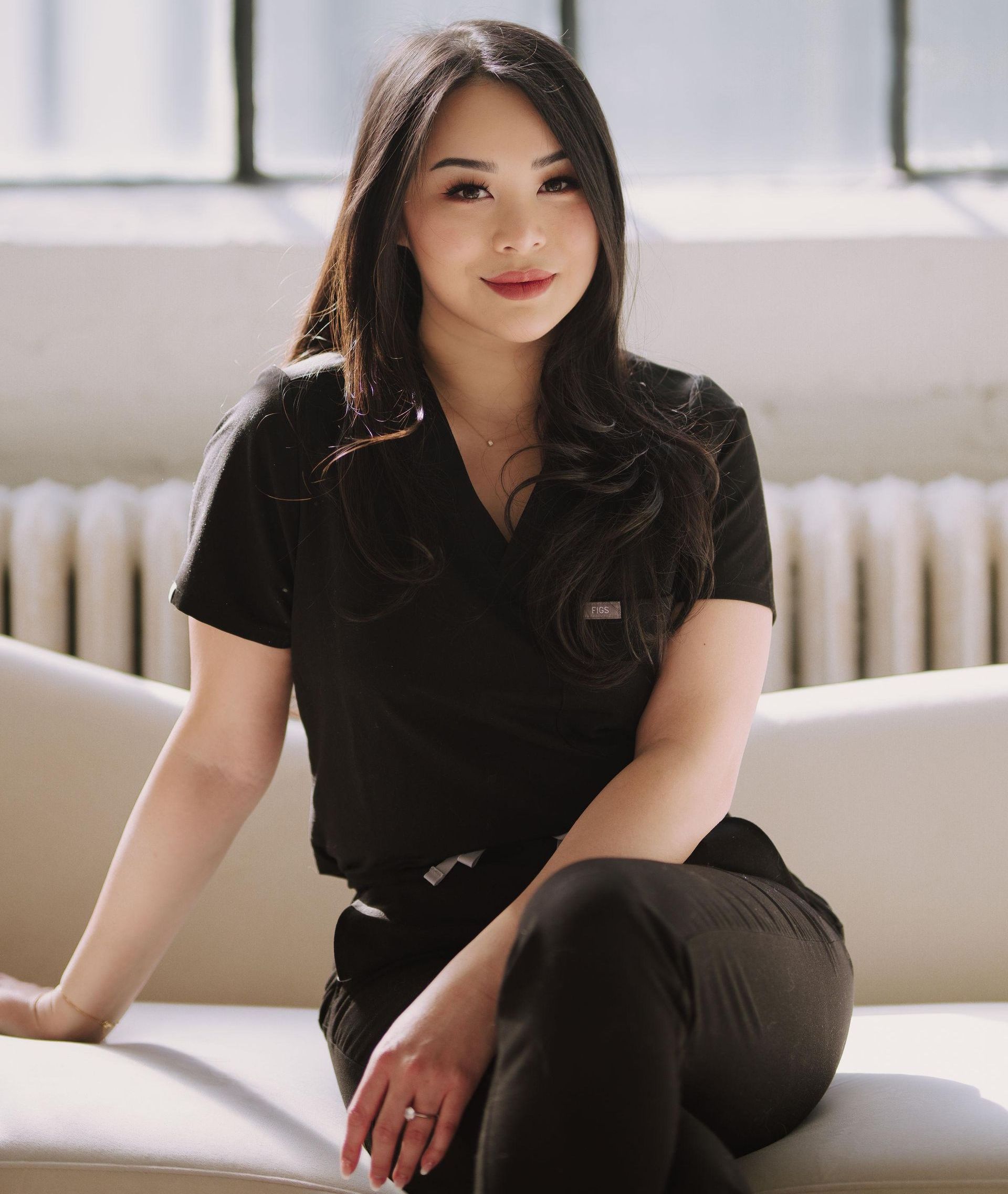 a woman in a black scrub top is sitting on a white couch